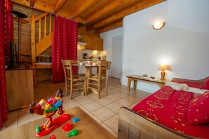 A cozy room with a wooden ceiling, a dining area with chairs and a table, and a bed with a red patterned bedspread. - Ski aux pieds | Proche du télésiège | Piscine (Saint-François-Longchamp)