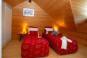 A cozy room with wooden walls and a sloped ceiling, featuring two beds with red bedding and heart patterns, a teddy bear on one bed, and a framed picture on the wall. - Ski aux pieds | Proche du télésiège | Piscine (Saint-François-Longchamp)