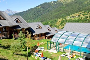 Un albergue con varias cabañas, un área de piscina cubierta y un paisaje montañoso de fondo.
