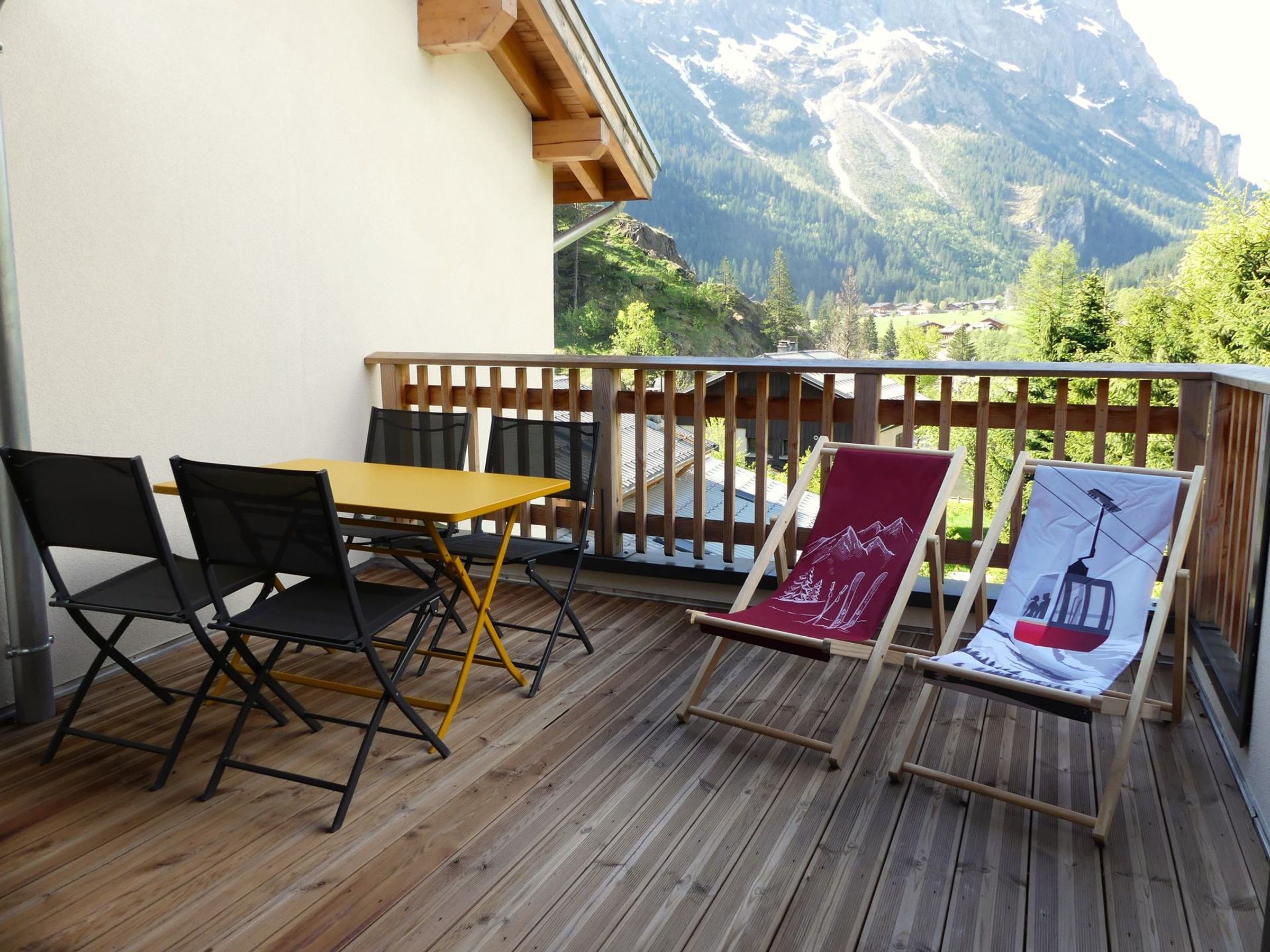 Une terrasse en bois avec une table et des chaises, une rambarde en bois et une vue sur la montagne.