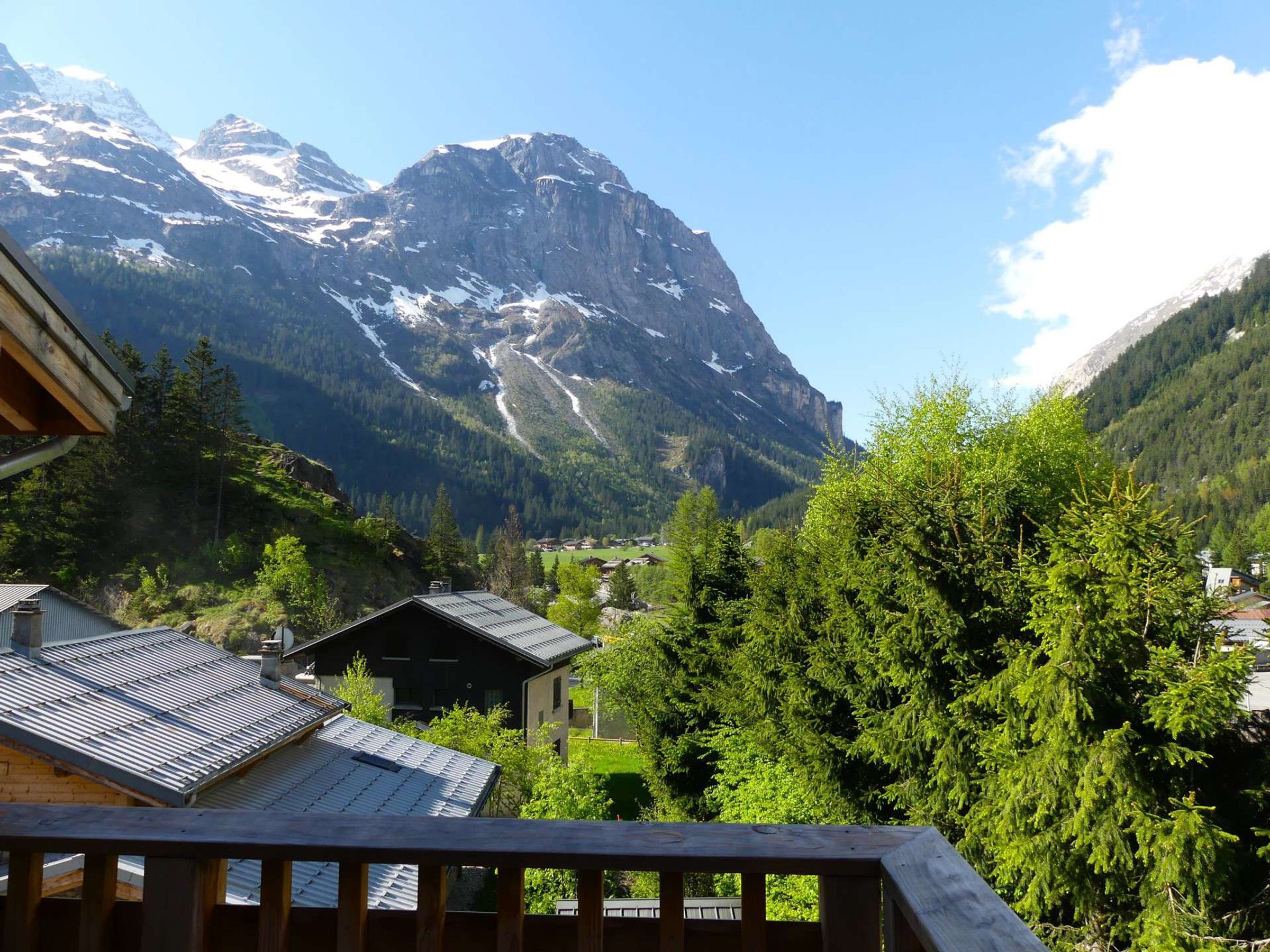A mountain landscape with a house and trees in the foreground.