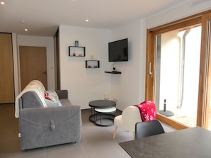 A modern living room with a grey sofa, a white armchair, a round table, and a flat-screen TV mounted on the wall. - Bright apartment with parking - 4 guests (Pralognan-la-Vanoise)