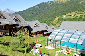A lodge with multiple cabins, a glass-enclosed pool area, and a mountainous backdrop. - Ski aux pieds | Piscine couverte | Station animée (Saint-François-Longchamp)
