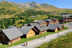Une rangée de cabanes en bois aux toits inclinés, se dressant sur un fond de montagnes et d’un ciel dégagé.