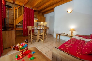A cozy room with a wooden ceiling, a dining area with chairs and a table, and a bed with a red patterned bedspread. - Ski aux pieds | Piscine couverte | Station animée (Saint-François-Longchamp)