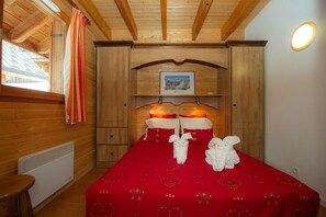 Ein Zimmer mit Holzboden, einem Bett, einem Fenster mit Vorhängen, einem Heizkörper und einem gerahmten Bild an der Wand.