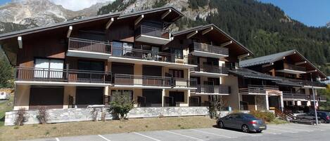 A multi-story hotel with balconies, a parking lot, and a mountainous backdrop.