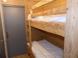 A bunk bed with a wooden headboard and a door to the left. - Cozy studio, pets welcome - 4 guests (Pralognan-la-Vanoise)