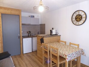 Eine kleine Küche mit einem Holztisch und Stühlen, einer Uhr an der Wand und einem kleinen Kühlschrank.