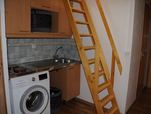 Ett kök med tvättmaskin, mikrovågsugn och en trästege som står lutad mot väggen.