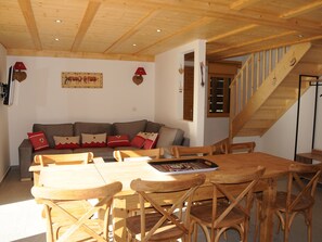 A wooden dining table with chairs, a sofa with cushions, a staircase, and a wall-mounted picture. - Spacious apartment with mezzanine - 8 guests (Pralognan-la-Vanoise)