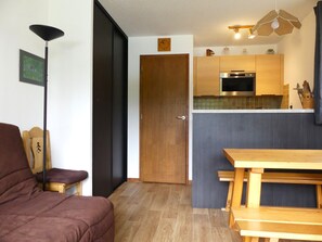 Un espacio habitable compacto con kitchenette, una zona de comedor con bancos, un sofá y una lámpara de pie.