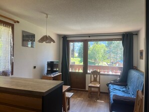 Een kamer met een houten eettafel, een televisie, een bank en een raam met gordijnen.