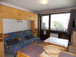 Ein Zimmer mit einer Sitzecke, einem kleinen Tisch, einem Korbwannenstuhl, Holzschränken und einem Fenster mit Blick.