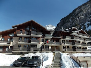 Ein mehrstöckiges Hotel mit Balkonen, einer Treppe, die zum Eingang führt, und einem verschneiten Berg im Hintergrund.