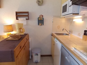 Cocina compacta con microondas, lavamanos y un pequeño cubo de basura.