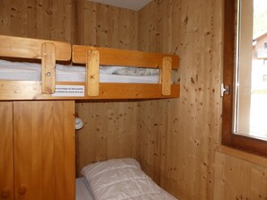 Une pièce dans une cabane en bois, avec des lits superposés, un petit placard et une fenêtre.
