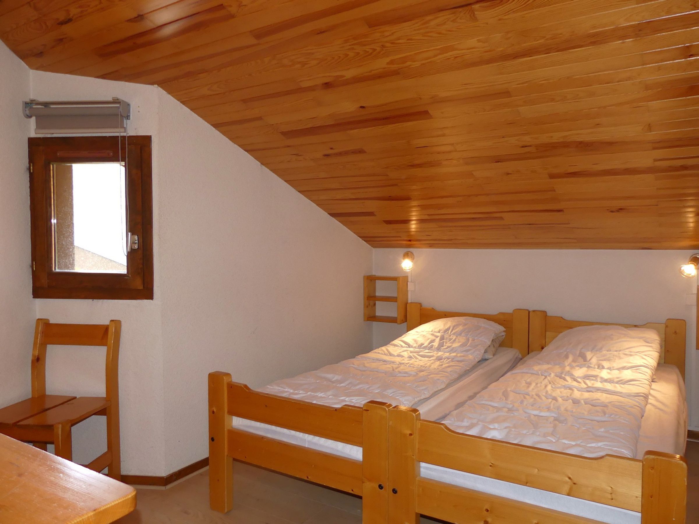 A single wooden bed with a headboard, a wooden chair, and a window with a wooden frame.