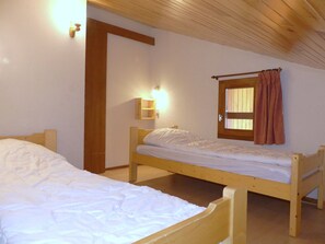 Ein Zimmer mit zwei hölzernen Betten, einer Holztür, einer Wandleuchte und einem Fenster mit Vorhang.