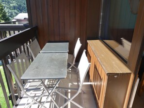 Ein Balkon mit einem Metalltisch und Stühlen, einem Holfachschrank und Blick auf ein bewaldetes Gebiet.