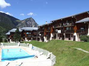 Ein Hotel mit mehreren Balkonen, einem Schwimmbad und einer Bergkulisse.