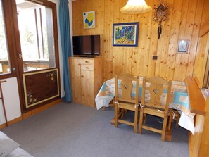 A wooden-paneled room with a bed, a table with chairs, a television, and wall art. - Ideal south-facing studio - 4 guests (Pralognan-la-Vanoise)