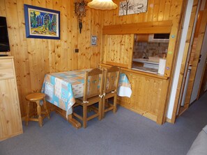 A wooden interior with a dining table set for two, a wooden cabinet, and a kitchenette area. - Ideal south-facing studio - 4 guests (Pralognan-la-Vanoise)