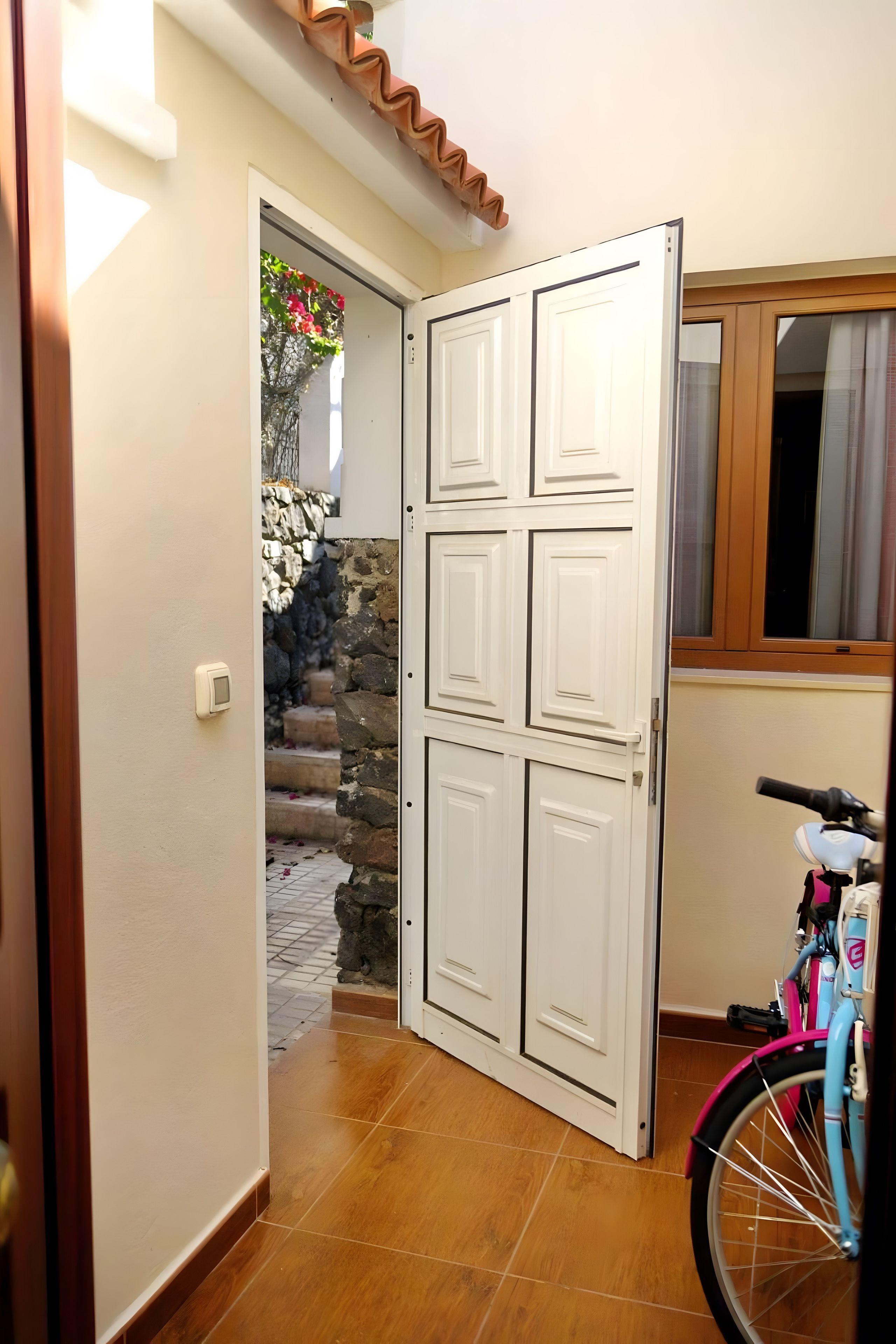 Een hal met een houten deur die naar een kamer leidt, een fiets en een stenen muur met treden.