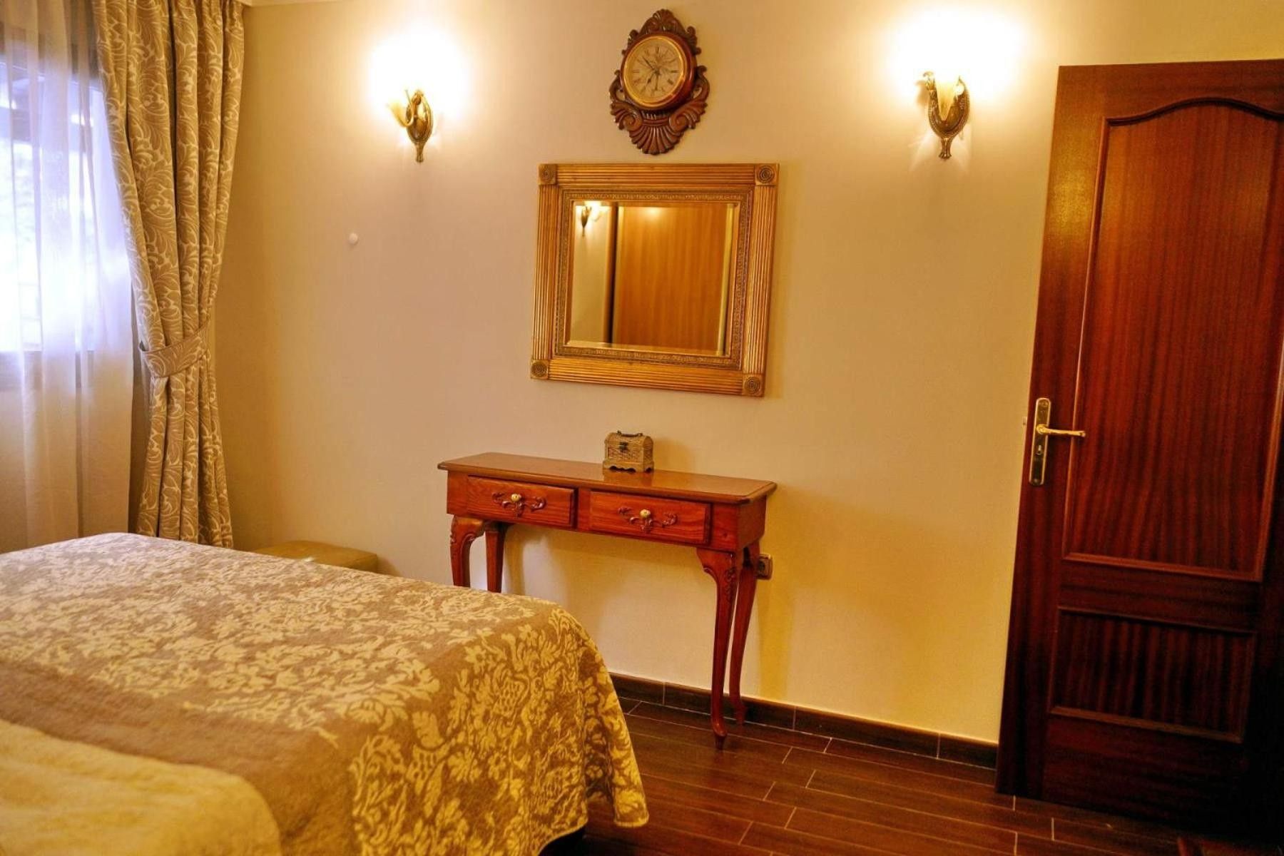 Een hotelkamer met een bed, een houten dressoir, een spiegel en een deur.