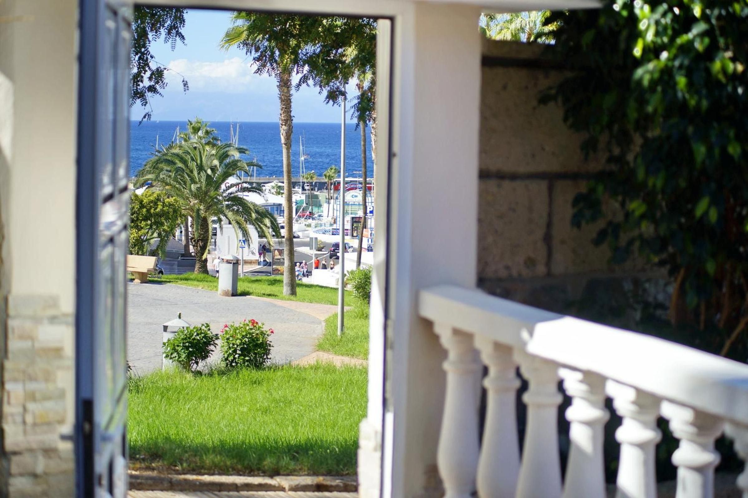 A view from a balcony overlooking a marina with boats, palm trees, and a clear sky.