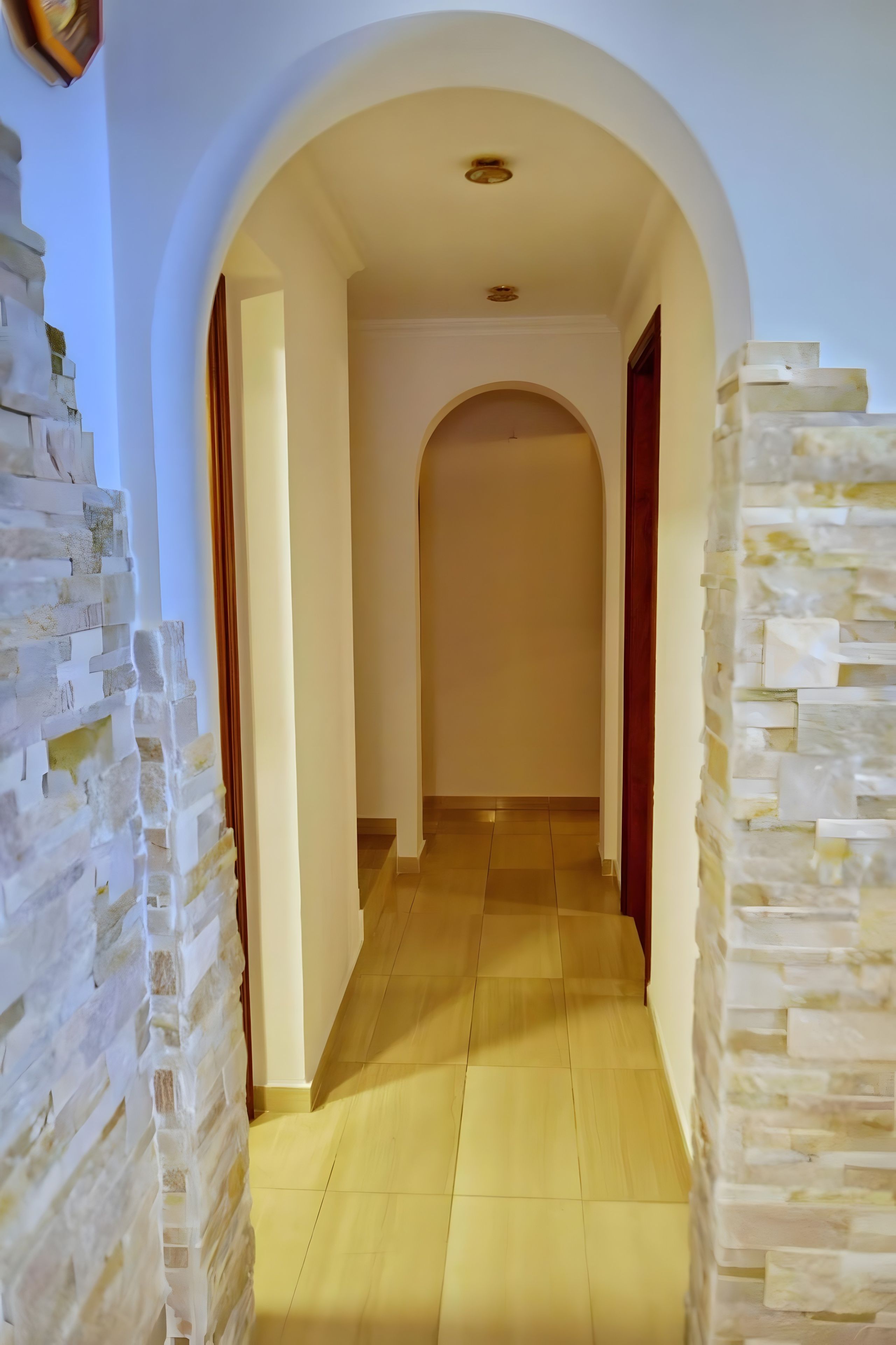 A hallway with a tiled floor, an arched doorway, and a stone wall on one side.