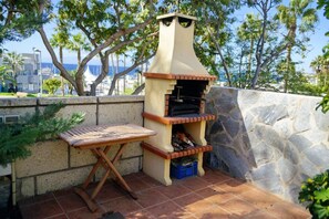 An outdoor barbecue grill with a stone wall and a wooden table.