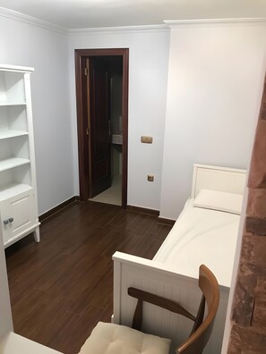 A room with a bed, a chair, a white wardrobe, and a door leading to another room.