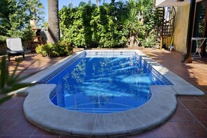 A swimming pool with a geometric tile pattern, surrounded by a patio area with chairs and a staircase.