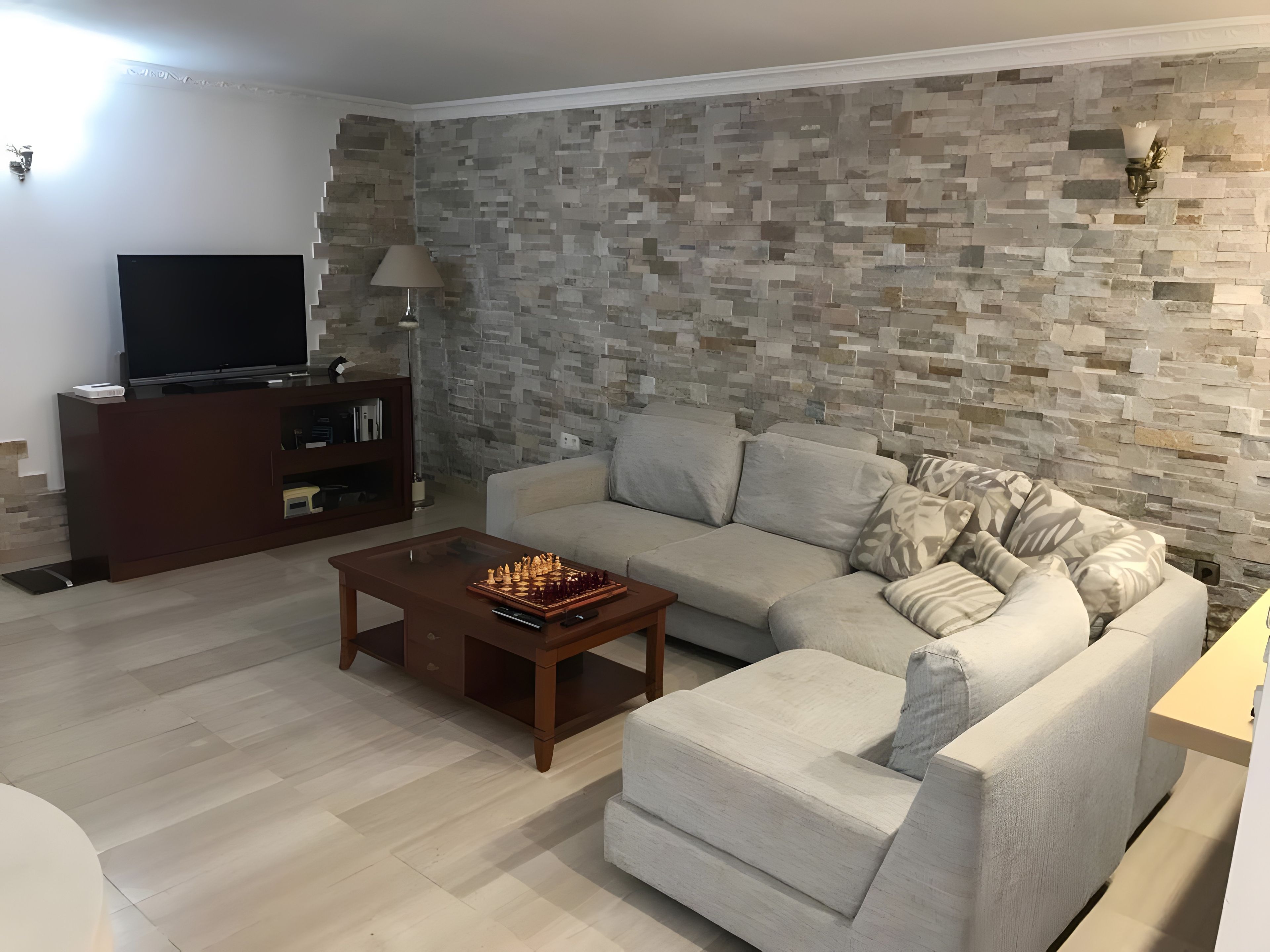 A living room with a stone wall, a sofa, a coffee table with a chess set, and a TV on a stand.