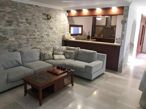 A modern living room with a sectional sofa, a coffee table, and a kitchen area with a stone backsplash.