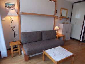 A small living room with a sofa, a wooden table, a lamp, a cabinet, and a mirror. - Studio in the heart of Pralognan - 4 guests (Pralognan-la-Vanoise)