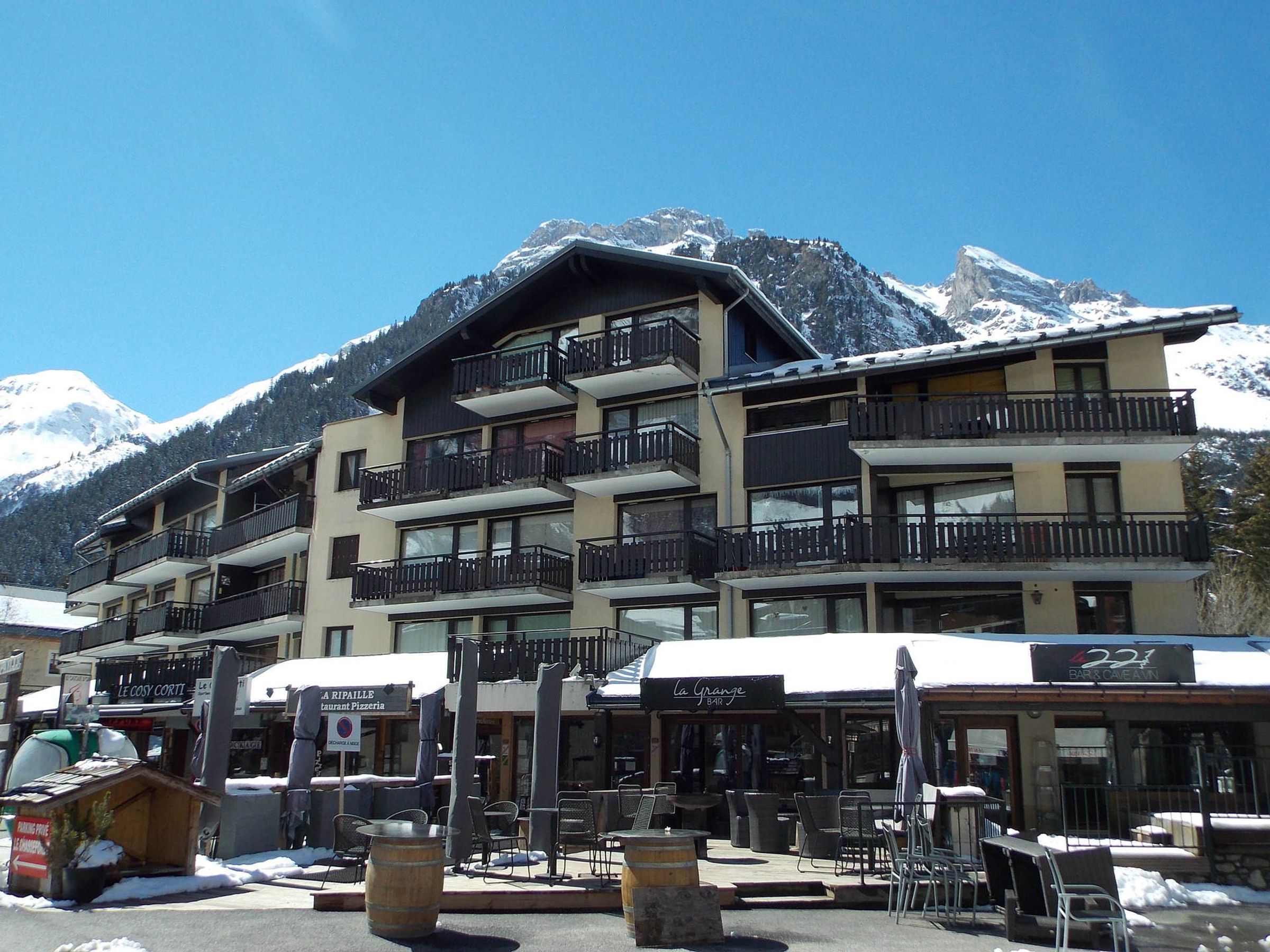 A multi-story hotel with balconies, outdoor seating, and a mountain backdrop.