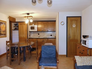 Ett kompakt kök med träskåp, ett matbord och stolar. Här finns en mikrovågsugn, ett handfat och en klocka på väggen.