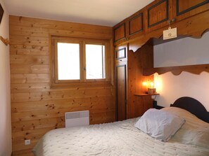 Ein Zimmer mit Holzwänden, einem Bett, einem Fenster und einem Wandheizgerät.