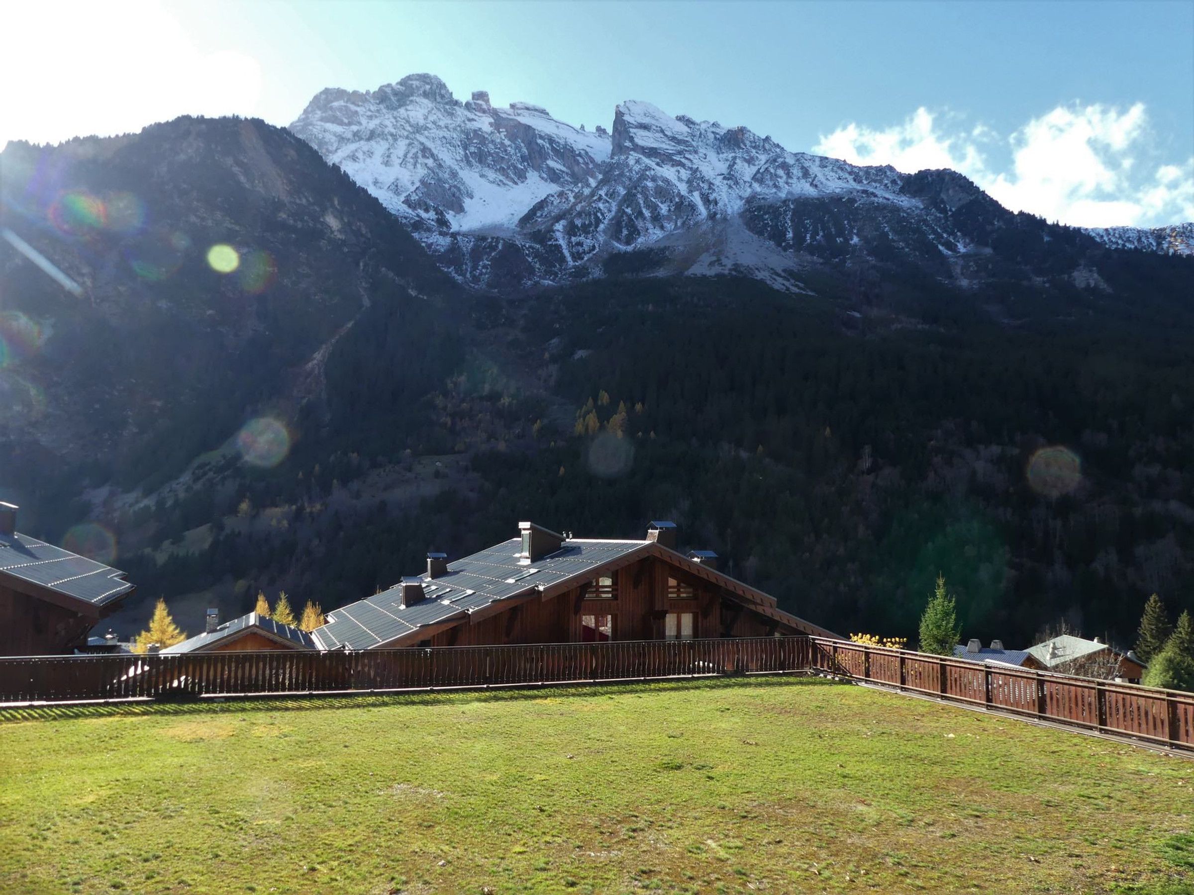 A mountain lodge with a wooden exterior, a fenced yard, and a view of snow-capped mountains.