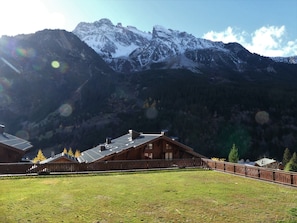 Eine Berglodge mit Holzbalkon, einem eingezäunten Garten und Blick auf schneebedeckte Berge.