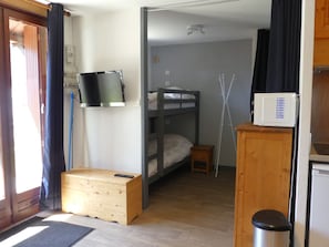 A compact room with a bunk bed, a television mounted on the wall, a microwave, and a small wooden cabinet. - Central studio cabin, pets welcome - 4 guests (Pralognan-la-Vanoise)