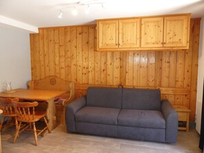 A room with a wooden wall, a sofa, a dining table with chairs, and a cabinet. - Central studio cabin, pets welcome - 4 guests (Pralognan-la-Vanoise)
