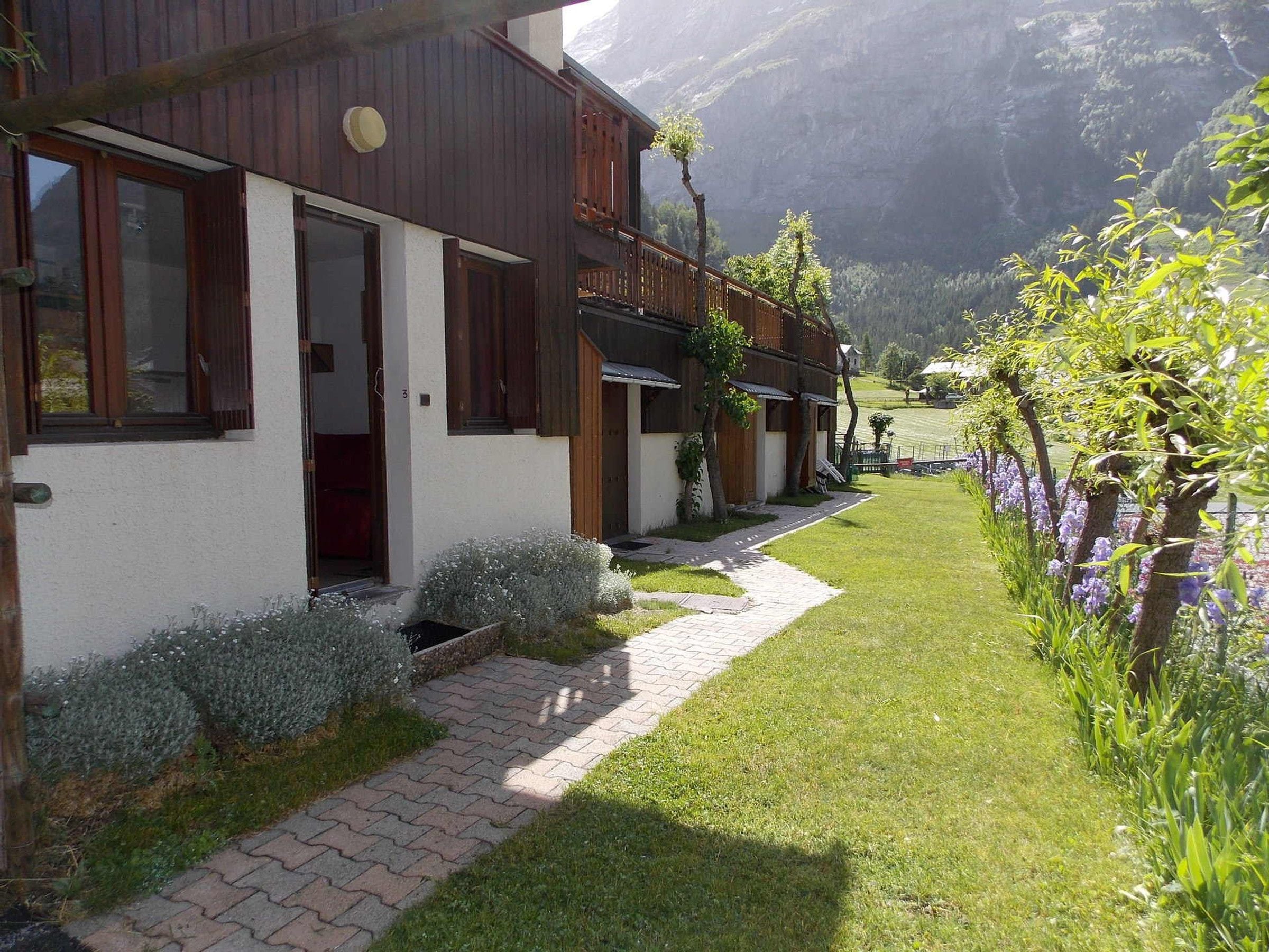 Un bâtiment à la façade en bois, un chemin pavé et un jardin agrémenté de fleurs violettes.
