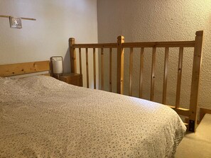 A bedroom with a wooden headboard, a bed with a speckled bedspread, a bedside table with a lamp, and a wall-mounted picture. - Apartment near slopes - 4 guests (Pralognan-la-Vanoise)