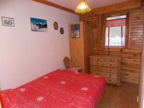 Ein Schlafzimmer mit einem hölzernen Kopfende, einer roten Bettdecke, einer Holzkommode und einem Fenster mit Blick.