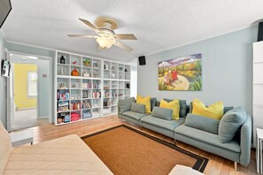 Ein Wohnzimmer mit einer Couch, einem Bücherregal, einem Gemälde und einem Deckenventilator.