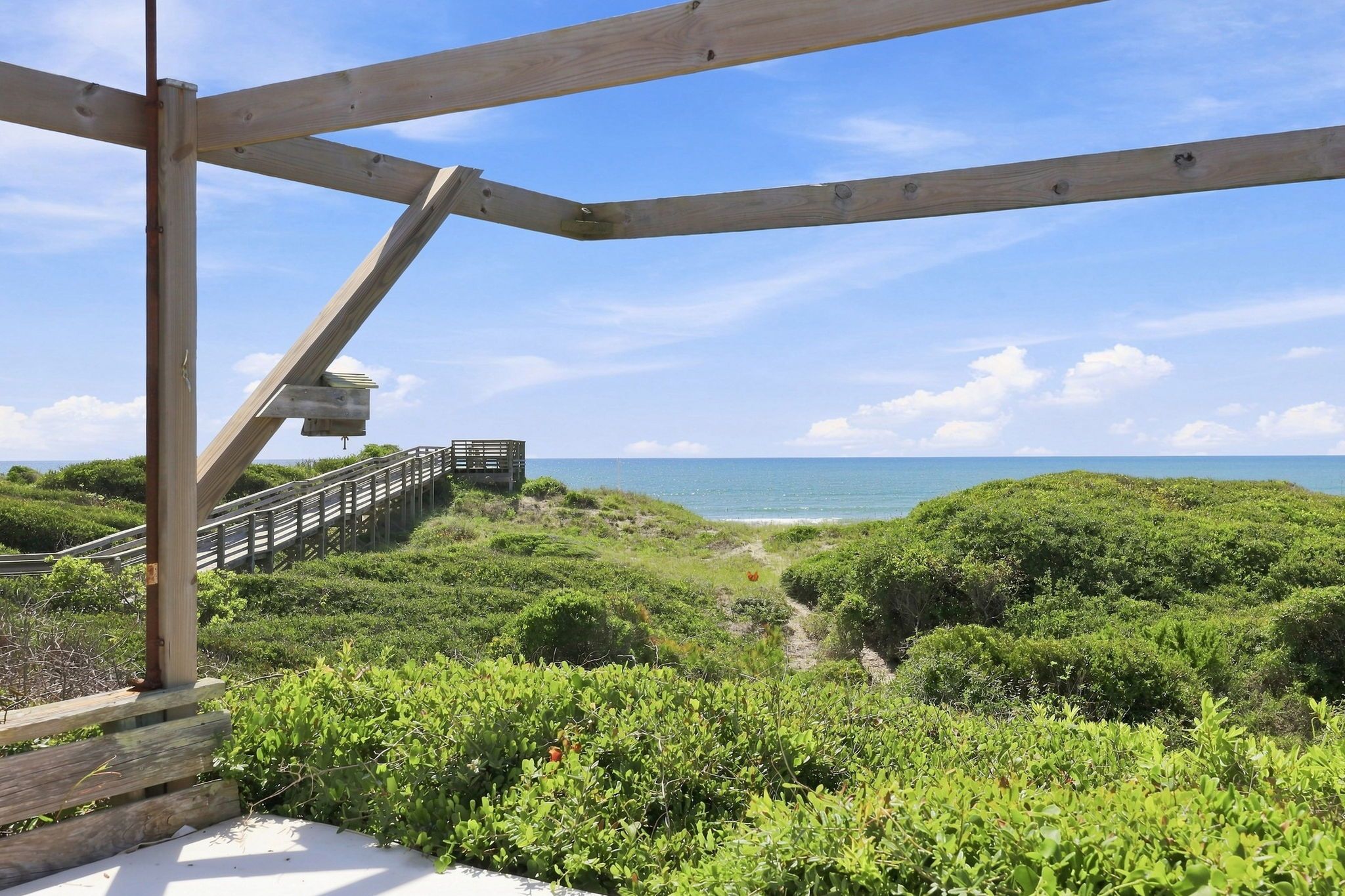 A wooden deck with a view of the ocean and a path leading to a beach.