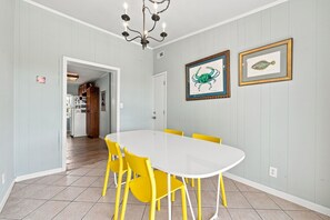 Ein Essbereich mit einem weißen Tisch, gelben Stühlen, einer Chandelierleuchtre und gerahmten Bildern an der Wand.